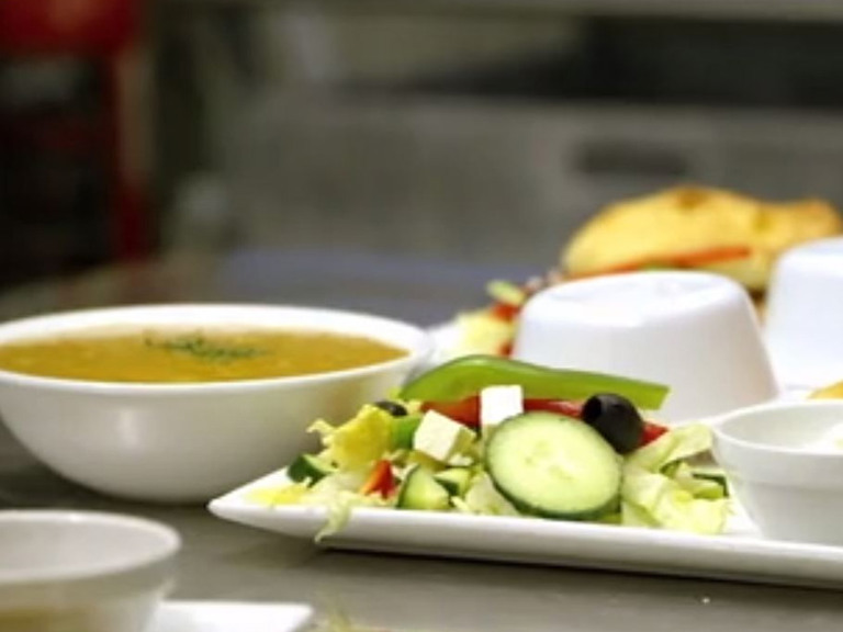 En hvit tallerken med salat ved siden av suppeskåler.