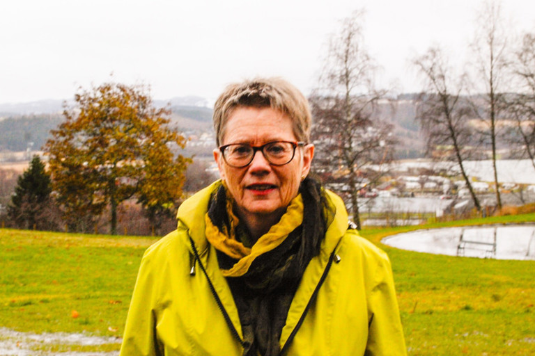 En kvinne i gul jakke står på en åker.