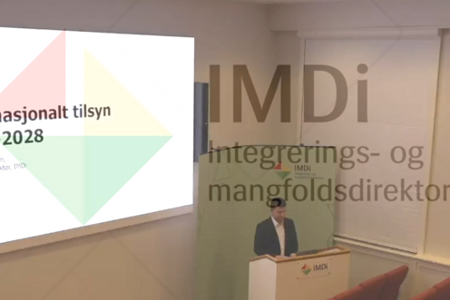 En mann som står på et podium foran et projektorskjermbilde.