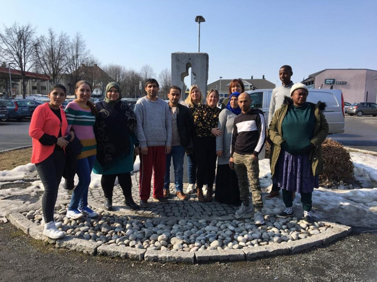 En gruppe mennesker som står foran et skilt.