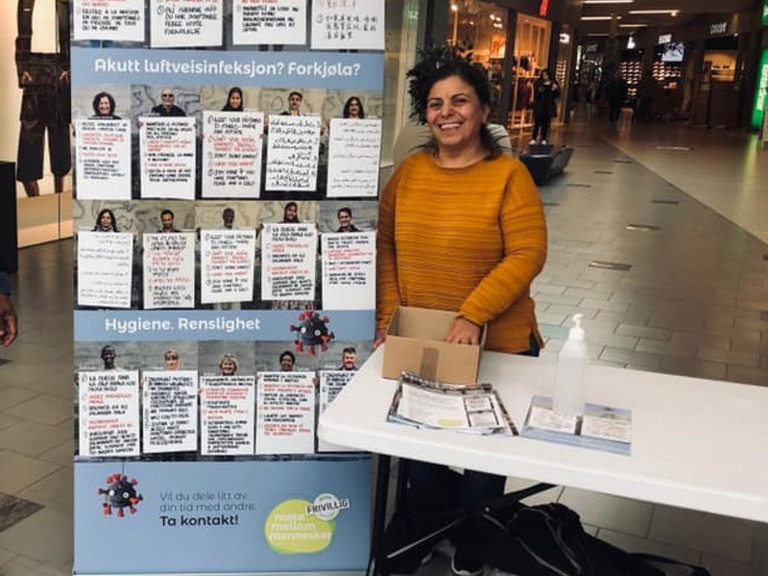 En kvinne står ved siden av et bord med et skilt på.