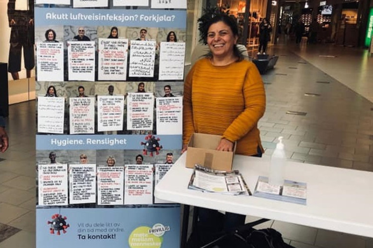 En kvinne står ved siden av et bord med et skilt på.